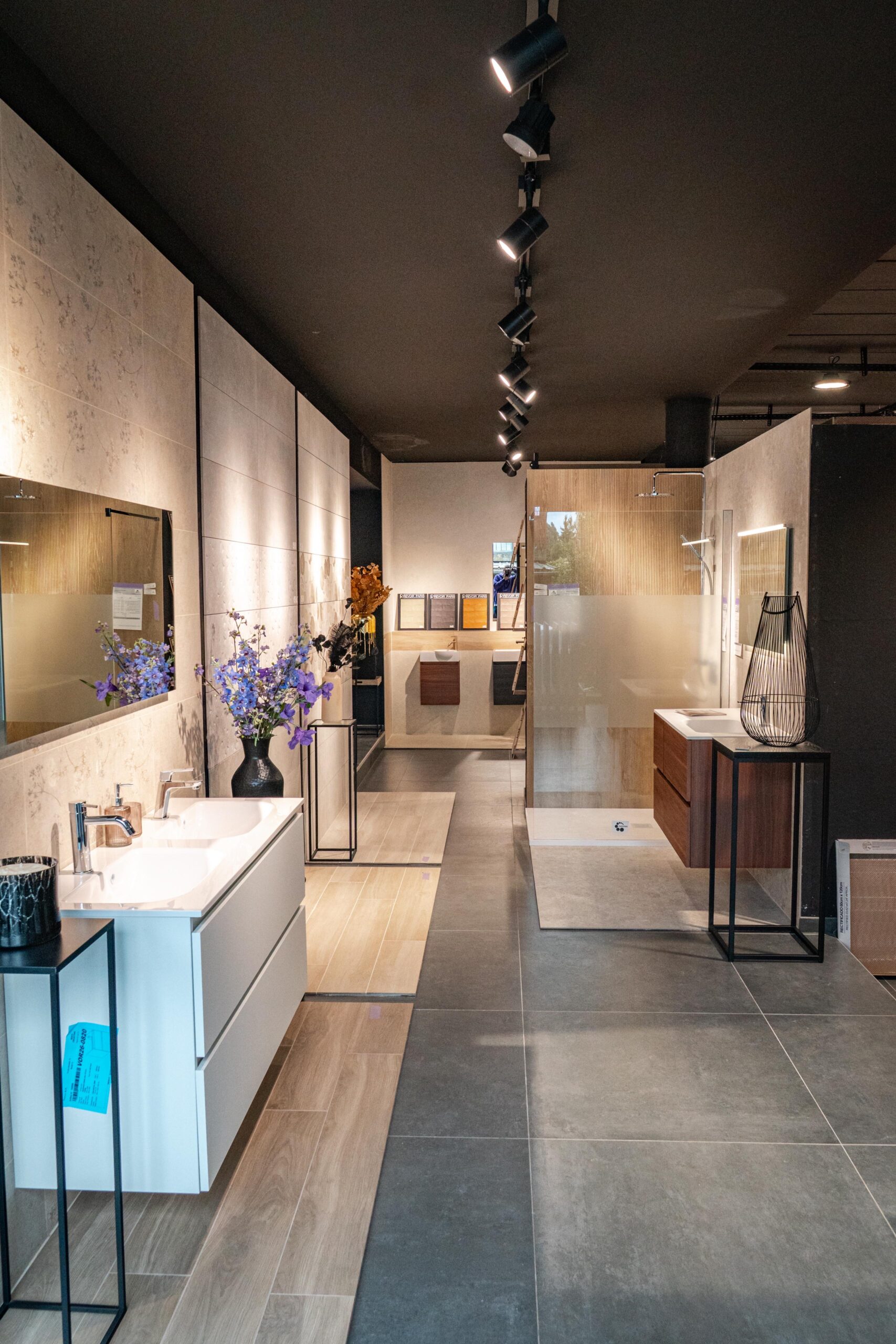 Allée du showroom bordée de meubles vasques et de miroirs, sous un éclairage sur rails.