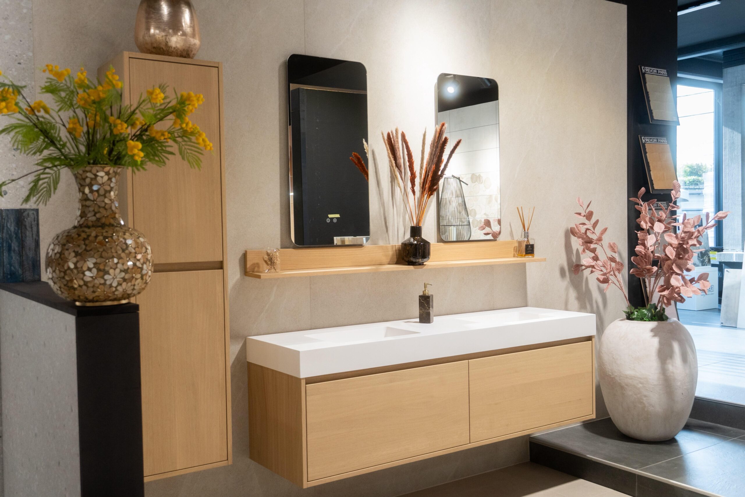 Meuble vasque suspendu effet bois clair, avec vasque blanche, deux miroirs verticaux et compositions florales.